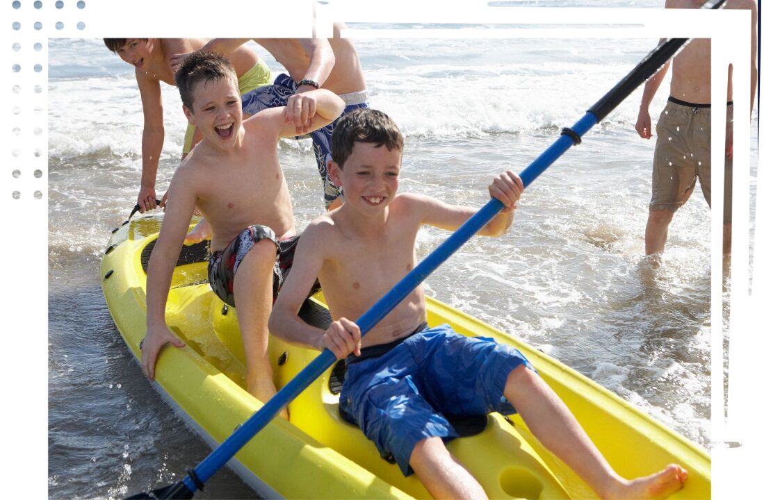 Two boys are paddling a canoe on the beach.